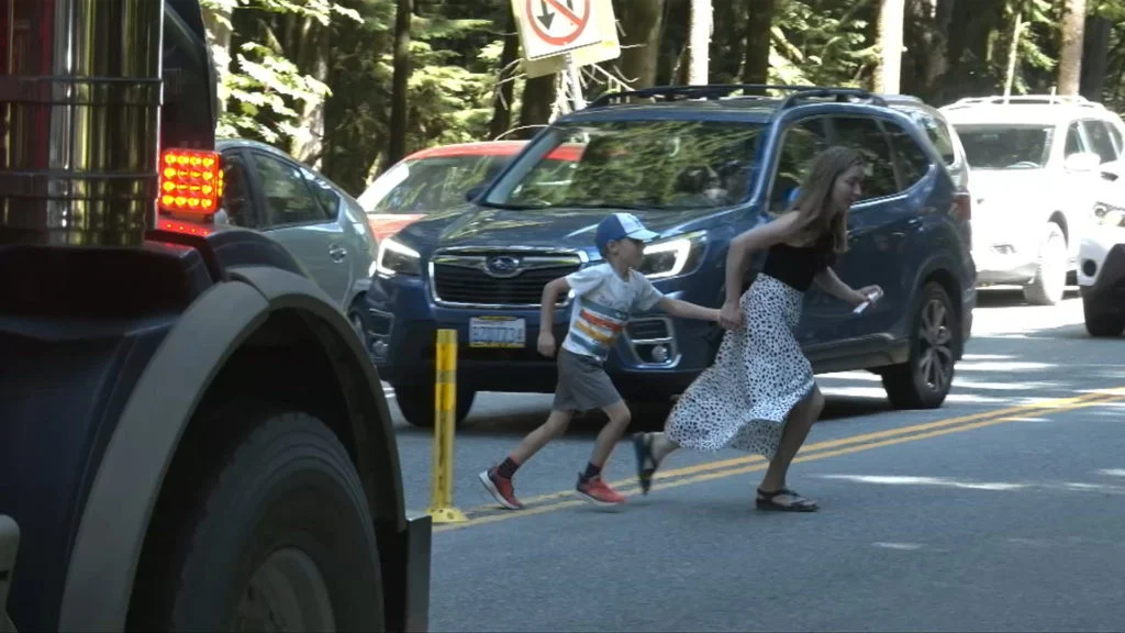 A young boy and his mother run between cars across the parking lot in Cathedral Grove.